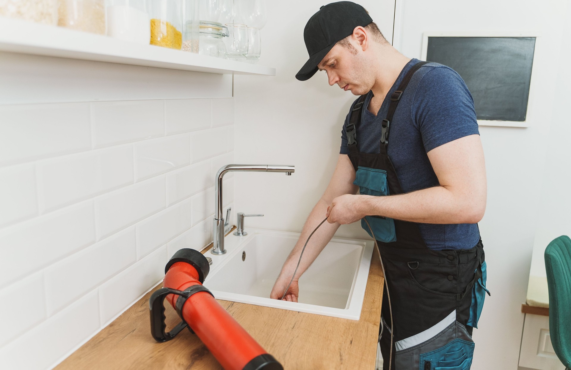 Plumber using drain snake to unclog kitchen sink.